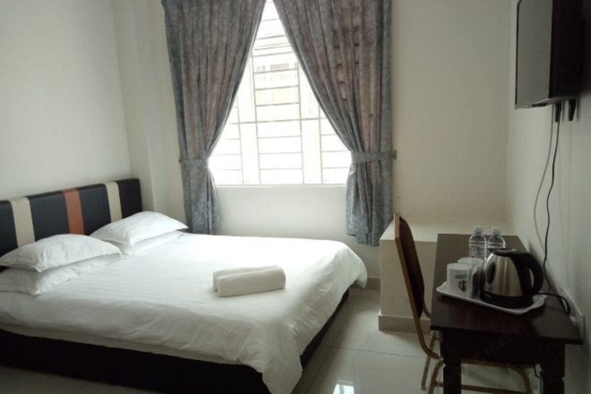 A hotel room with a bed, a desk with a kettle, and a TV on the wall.