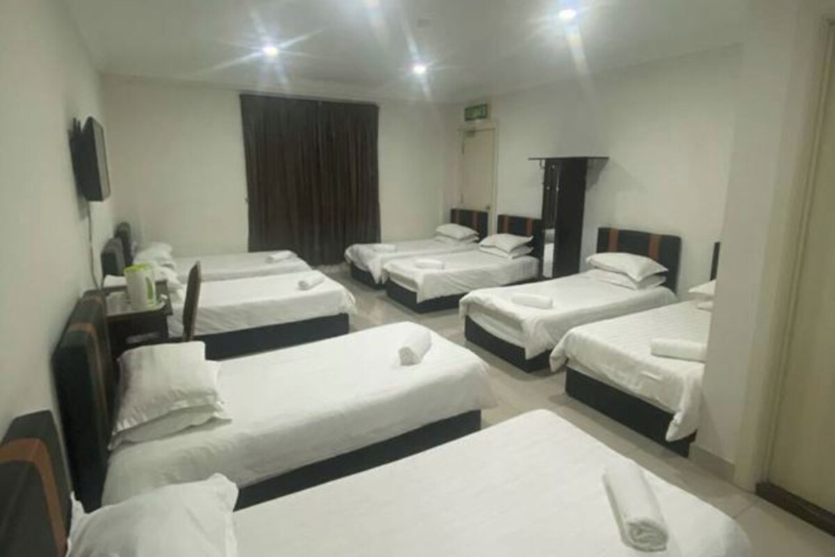 A hotel room with four single beds, a desk with a chair, a TV mounted on the wall, and a window with curtains.