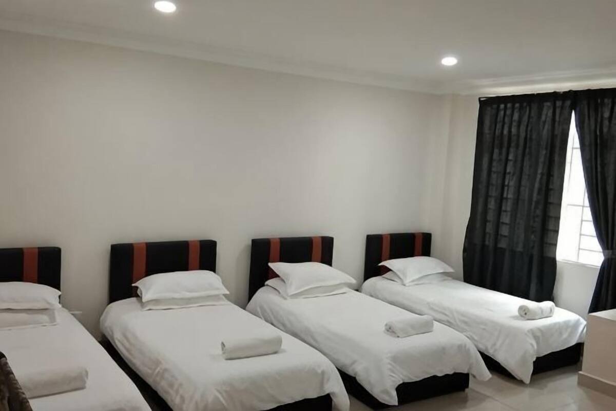 Una habitación de hotel con cuatro camas individuales, una ventana con cortinas y una pared blanca.