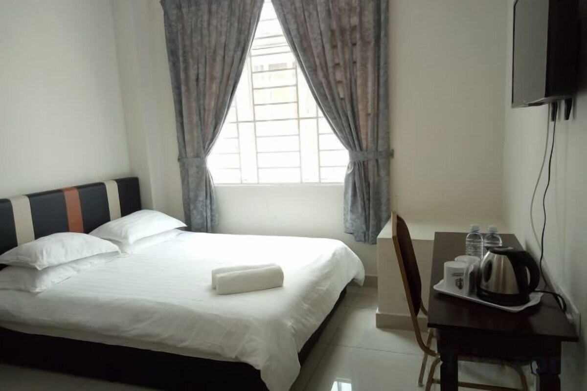 Une chambre d’hôtel avec un lit, un bureau doté d’une bouilloire et une fenêtre avec des rideaux.