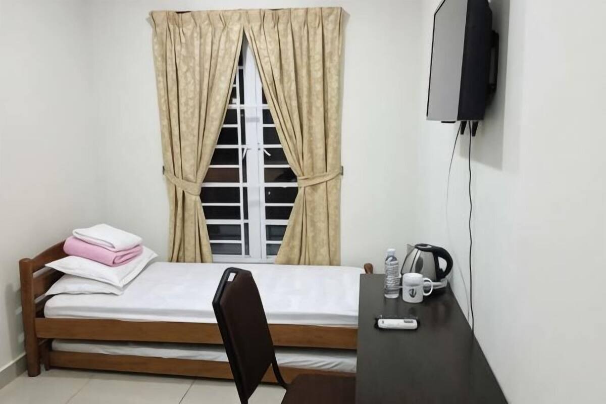Una habitación pequeña con una cama, un escritorio con hervidor, una silla y un televisor montado en la pared.