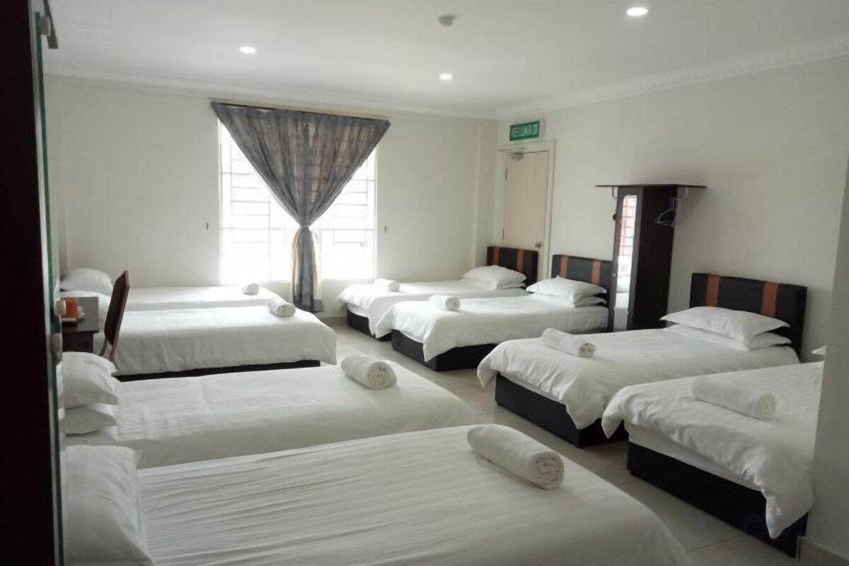 Habitación de hotel con cuatro camas dispuestas en fila, un ventanal con cortinas y una puerta con un letrero de salida.