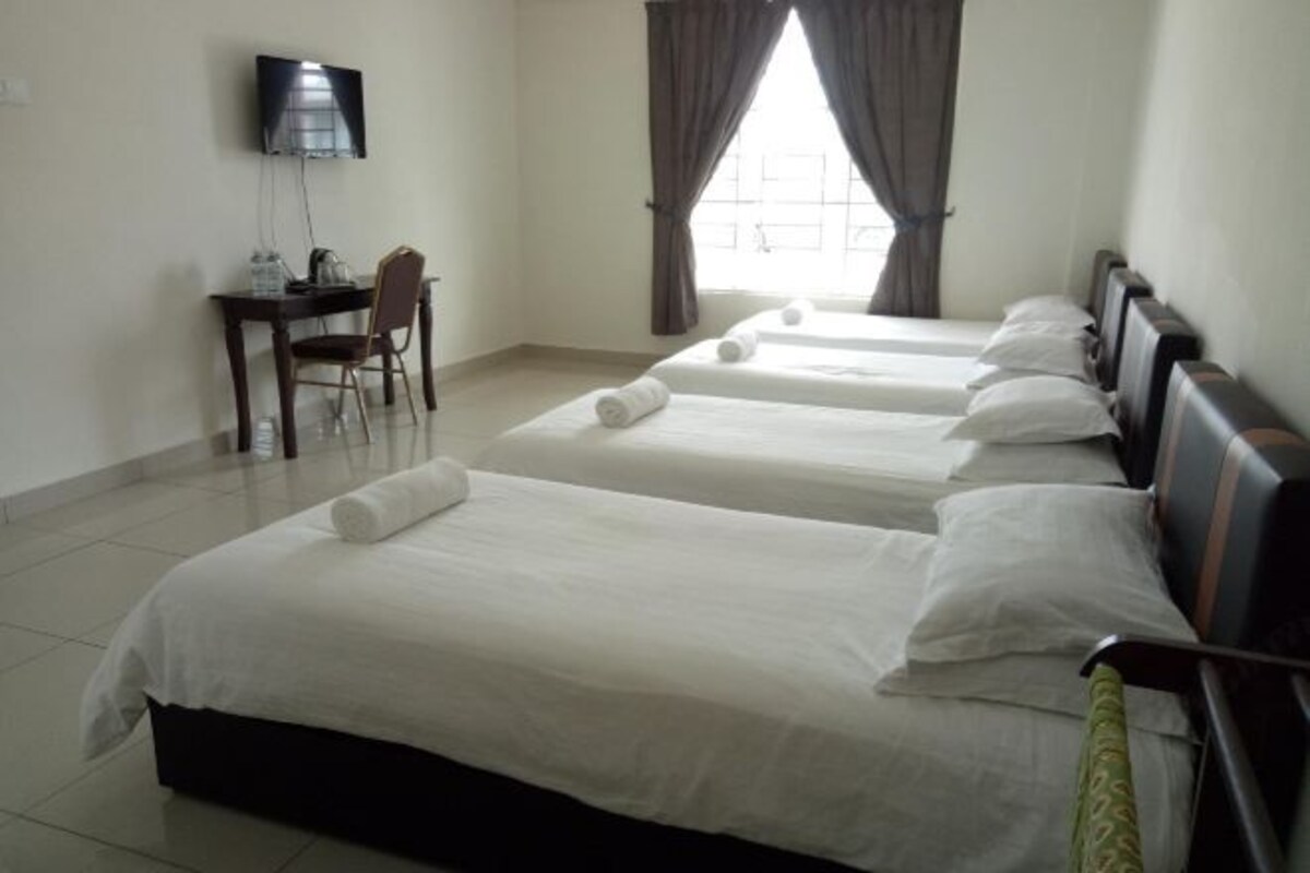 A hotel room with four single beds, a desk with a chair, a television, and a window with curtains.