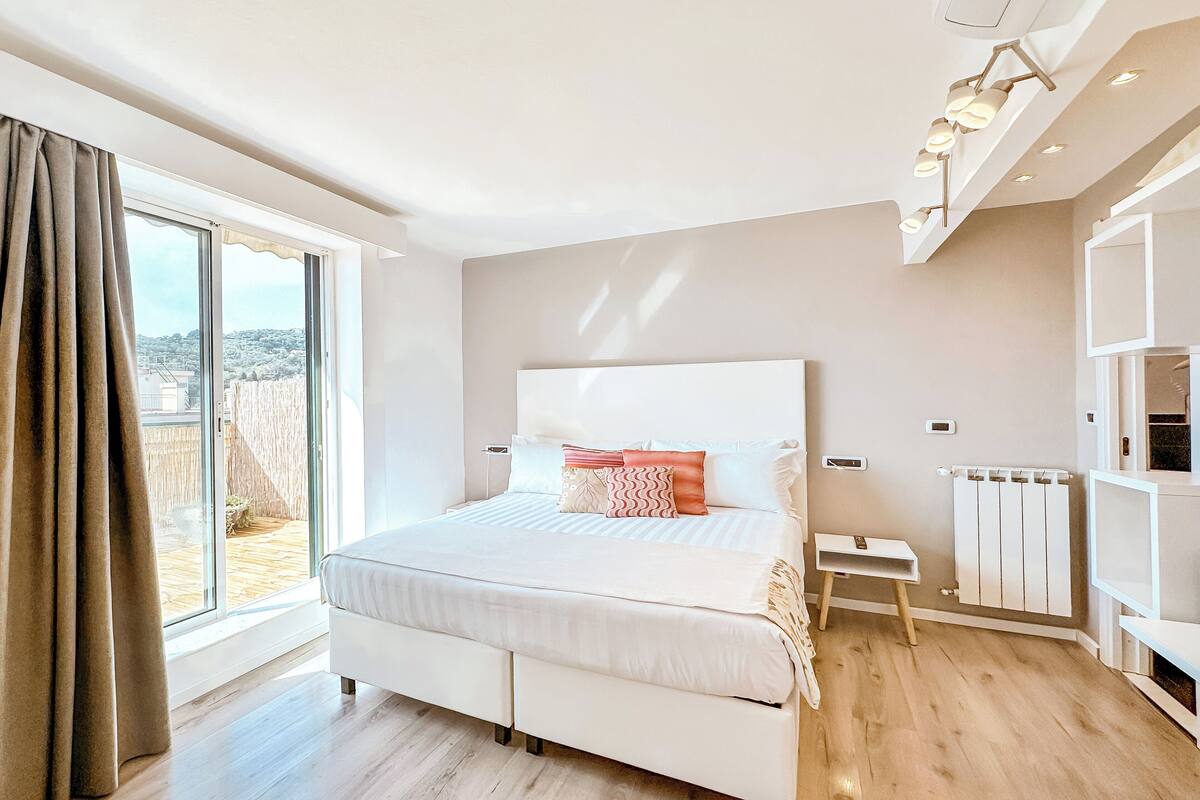 A modern bedroom with a large bed, a view through a sliding door, and a built-in shelf with lighting.