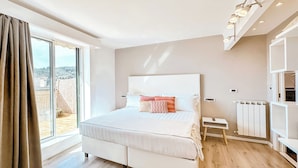 A modern bedroom with a large bed, a view through a sliding door, and a built-in shelf with lighting.