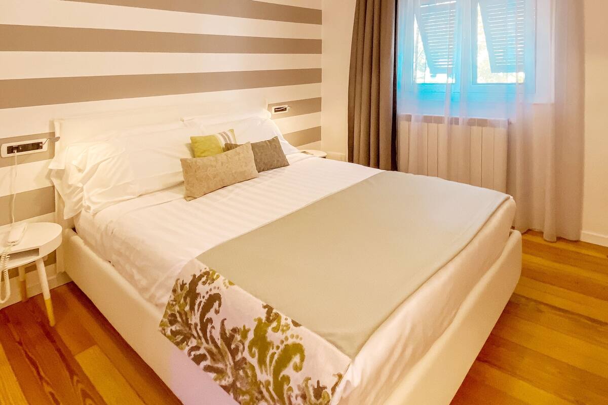 A neatly arranged bedroom with a large bed, bedside tables, a hanging lamp, and a window with curtains.