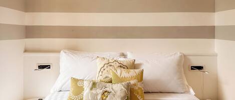 A hotel room with a striped wall design, a neatly made bed with multiple pillows, and bedside tables with remote controls.