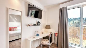 Une chambre d’hôtel moderne équipée d’un lit, d’un bureau, d’une chaise, d’une télévision, d’une lampe et d’une grande fenêtre donnant sur la ville.