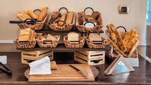 A display of various breads and cheeses on a wooden table with a cutting board and knife.