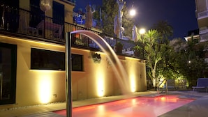 A pool area with a water feature, a balcony with outdoor seating, and a well-lit environment.