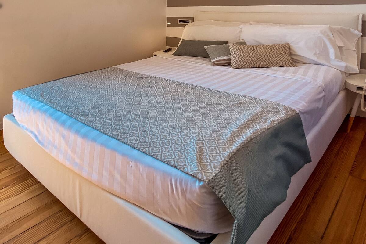 A neatly made bed with a patterned bedspread and pillows, a bedside table with a lamp, and a striped wall.