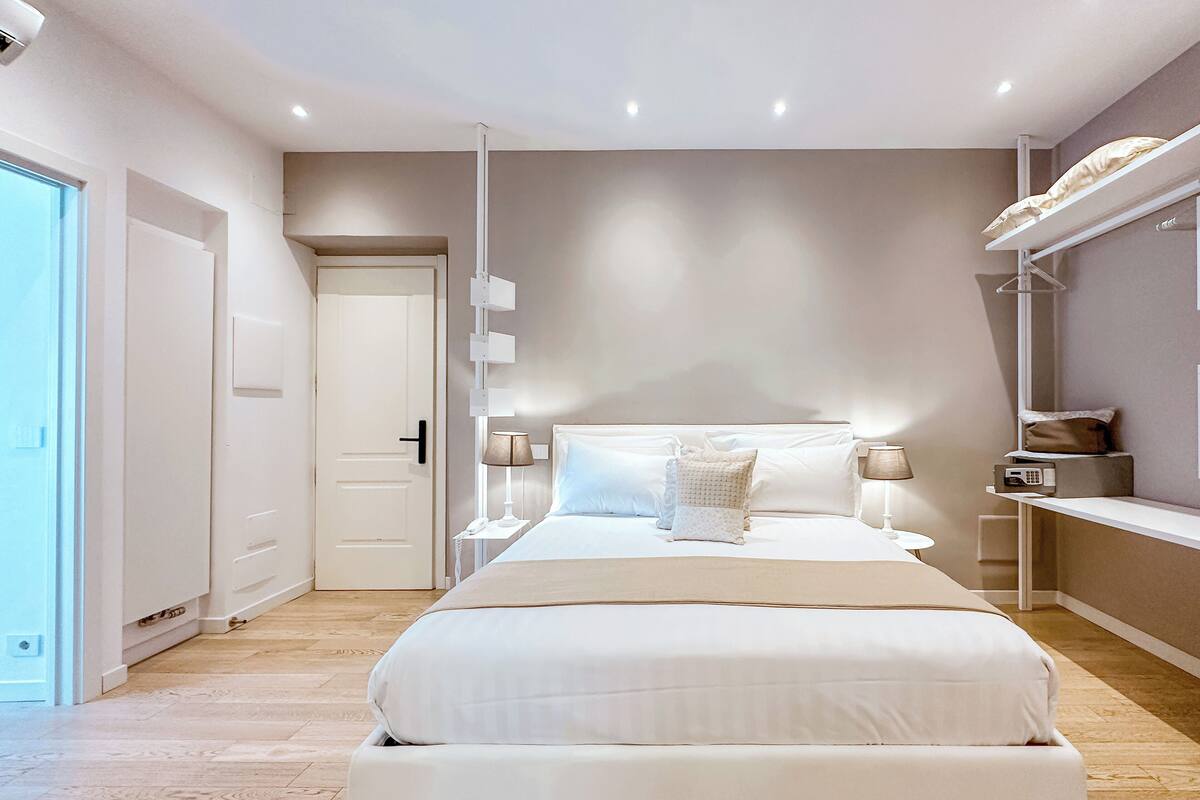 A modern bedroom with a large bed, bedside tables, a wardrobe, and a built-in bench with storage.