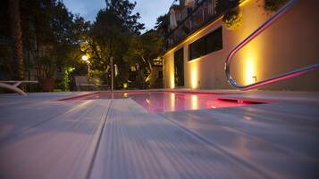 A swimming pool with a metal deck, surrounded by potted plants and outdoor furniture.