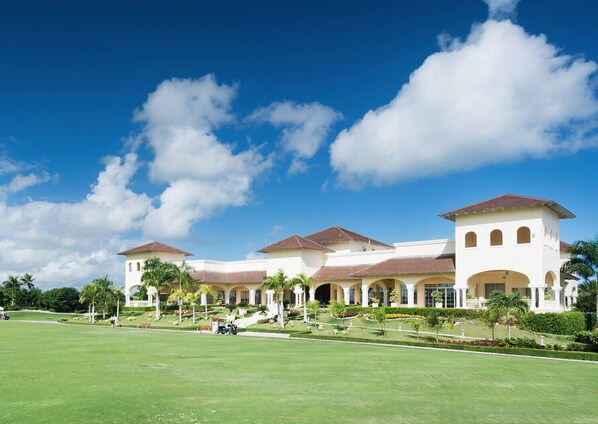 A large, multi-story building with a symmetrical facade, featuring a central courtyard with palm trees and a lawn.
