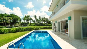 A swimming pool with a clear blue water, surrounded by a well-maintained lawn and palm trees.