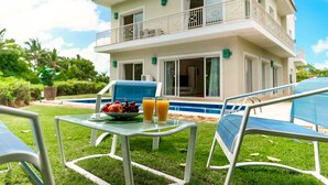 A two-story house with a pool, a dining table with fruit and juice, and outdoor seating.