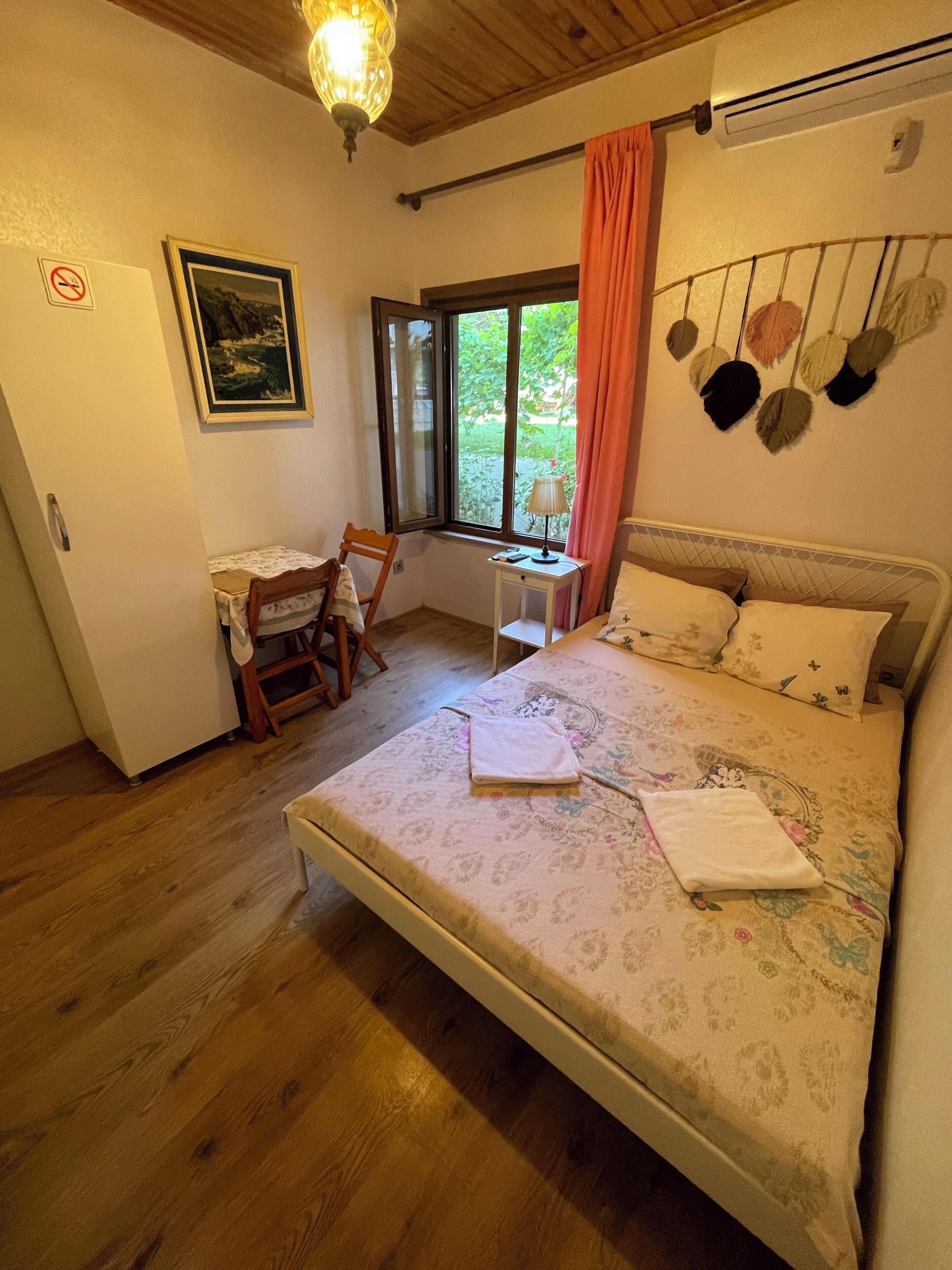 A bedroom with a bed, a desk, a chair, a window, and a wall-mounted decoration.