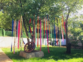 Un árbol con cintas de colores colgando de sus ramas y una rueda de madera sobre una base de piedra en una zona cubierta de césped.