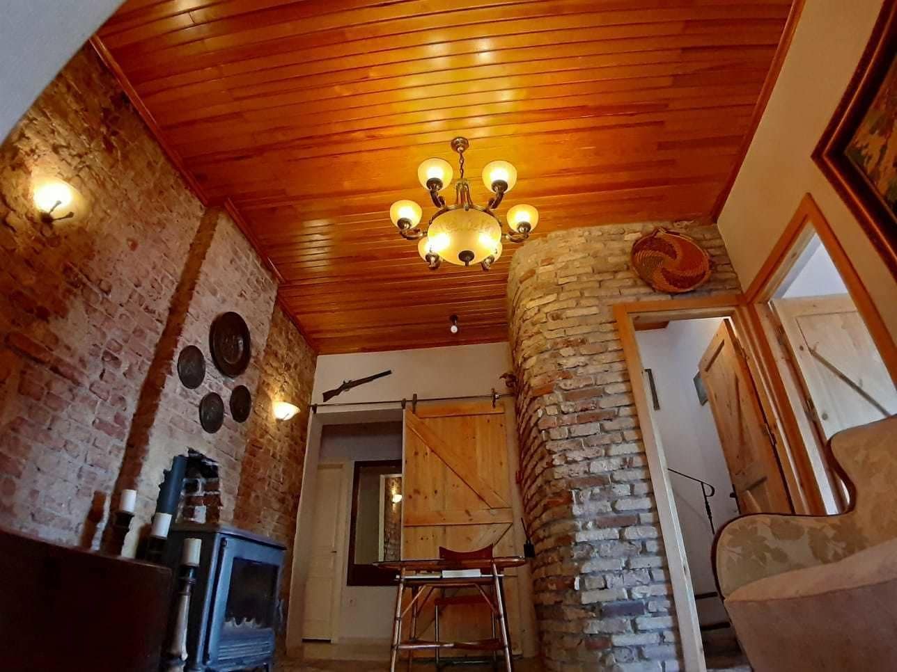 Un interior rústico con paredes de ladrillo visto, techo de madera y una araña.