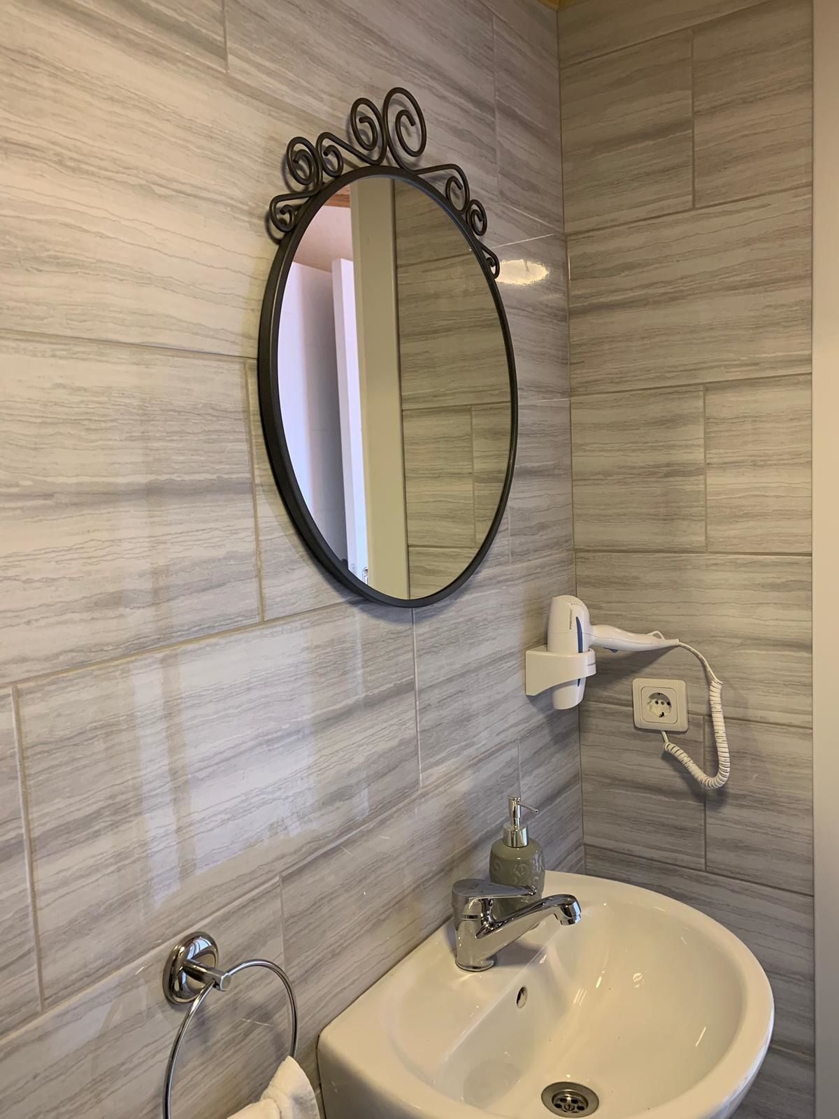 A bathroom with a round mirror, a white sink, and a towel rack.