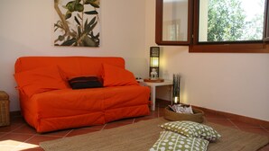 Una habitación con un sofá naranja, una cesta tejida y un cojín blanco y verde con lunares sobre un tapiz.