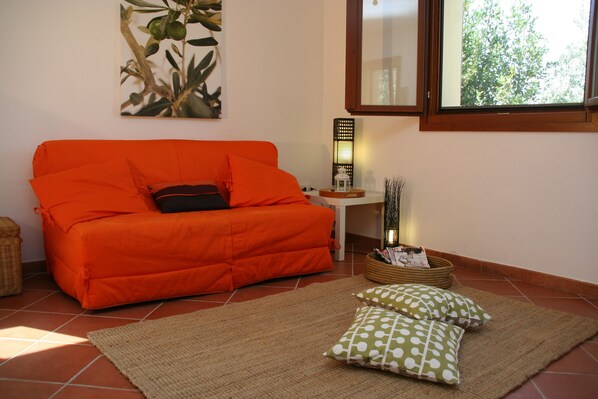 A room with an orange sofa, a woven basket, and a green and white polka dot pillow on a woven rug.
