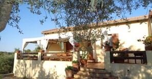 A two-story building with a white facade, terracotta roof tiles, and multiple potted plants.