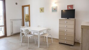 A room with a white table and chairs, a wooden cabinet, a television, and artwork on the wall. - N196 - Numana, delightful two-room apartment with garden and sea view (Numana)