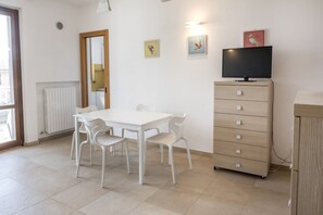 A room with a white table and chairs, a wooden cabinet, a television, and artwork on the wall.