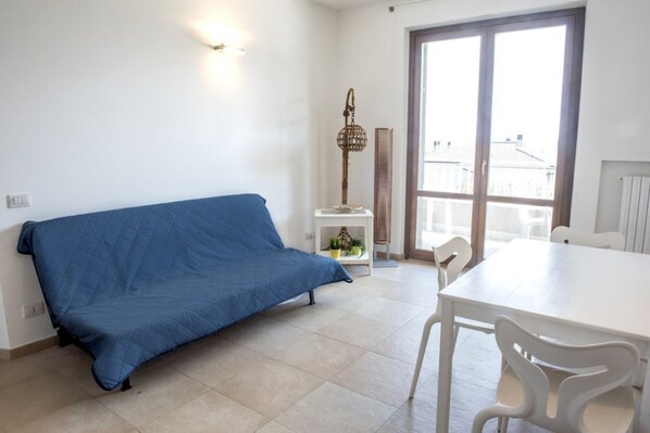 A room with a blue sofa, a white dining table, and chairs.