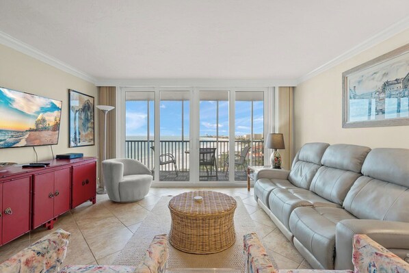A living room with a sofa, a red cabinet, a television, and a large window with a view of the beach.