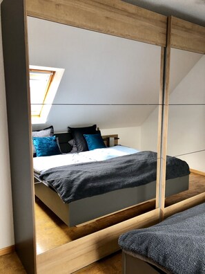 A bedroom with a bed, a skylight, and a mirrored wardrobe.