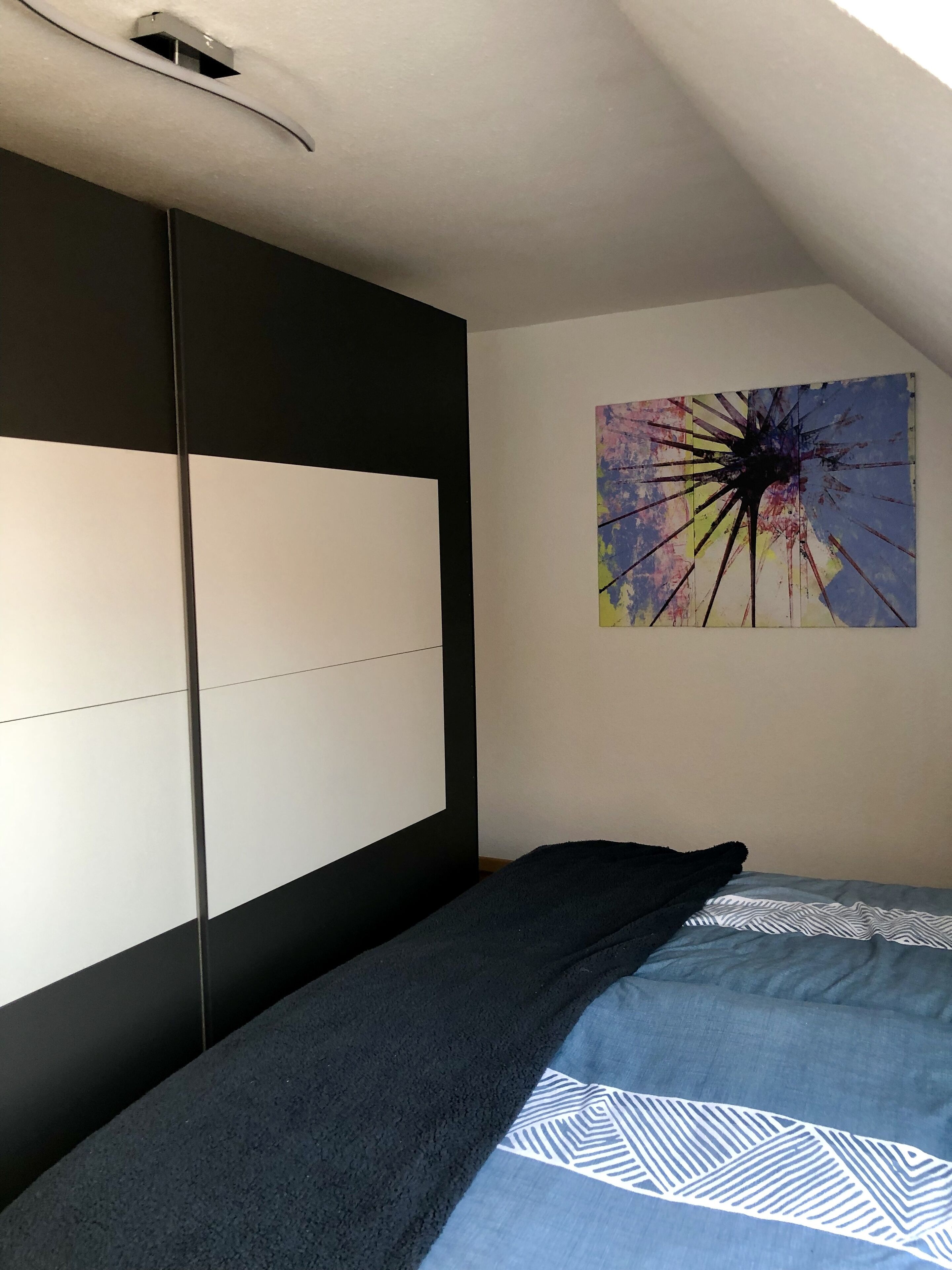 Makuuhuoneessa on mustavalkoinen sängynpääty, värikäs abstrakti maalaus seinällä ja kuviollinen vuodevaatesetti.
