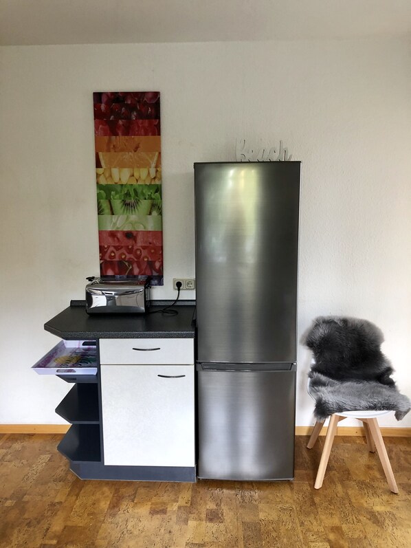 Una cuina moderna amb un frigorífic d'acer inoxidable, un taulell negre, un armari blanc i un quadre abstracte i colorit a la paret.