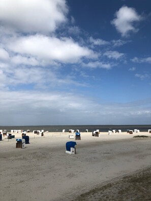 A beach with rows of beach chairs and umbrellas, a sandy shore, and a calm sea under a partly cloudy sky.