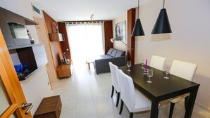 A modern dining area with a dark wooden table, white chairs, and black pendant lights. - MALDIVAS Apartments (La Pineda)