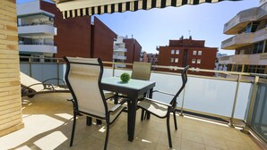 A balcony with a table and chairs, a small plant, and a view of surrounding buildings. - MALDIVAS Apartments (La Pineda)