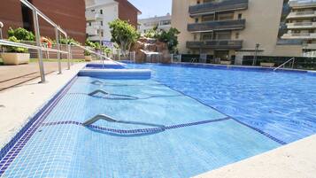 A swimming pool with clear blue water, surrounded by a sandy deck.