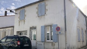 Un edificio de fachada blanca y contraventanas azules, con un cartel de prohibido estacionar.