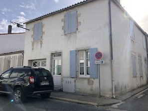 Un edificio de fachada blanca y contraventanas azules, con un cartel de prohibido estacionar.