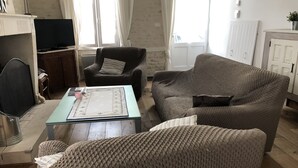 Una sala de estar con un sofá, un sillón y una mesita de centro. Hay un televisor sobre un mueble bajo y un aparador con una planta.