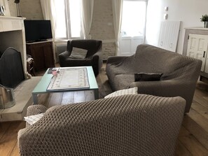 Una sala de estar con un sofá, un sillón y una mesita de centro. Hay un televisor sobre un mueble bajo y un aparador con una planta.