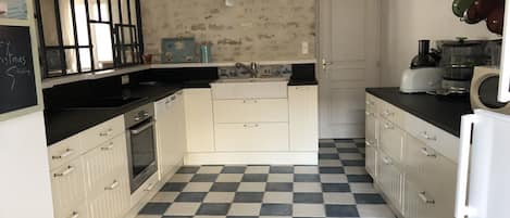 Une cuisine de taille modeste, avec des meubles blancs, un carrelage noir et blanc à motifs et des appareils électroménagers de base.