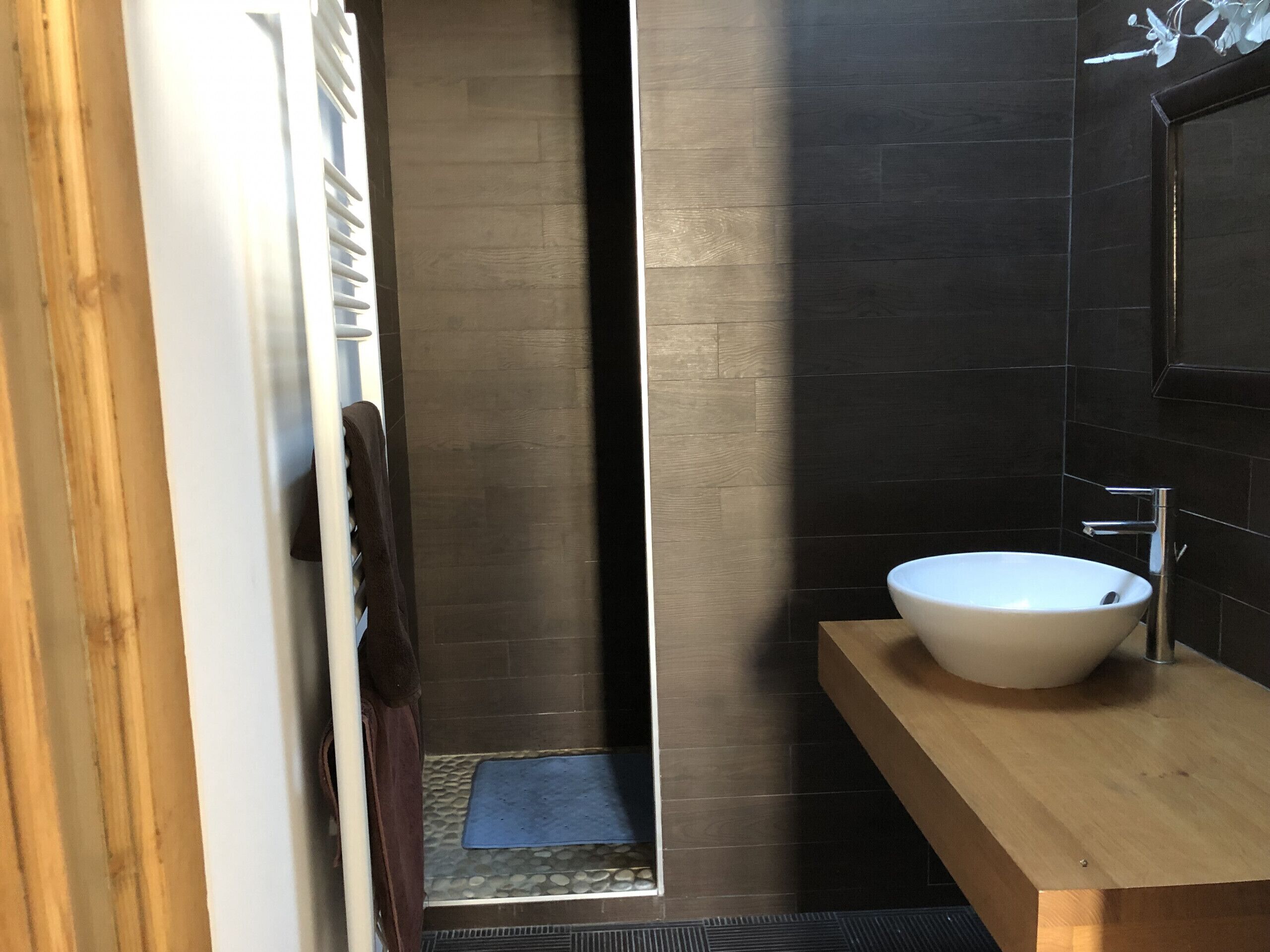 Une salle de bain moderne avec un grand lavabo blanc, des murs recouverts de carreaux foncés et un meuble-lavabo en bois.