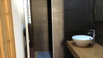 Une salle de bain moderne avec un grand lavabo blanc, des murs recouverts de carreaux foncés et un meuble-lavabo en bois.