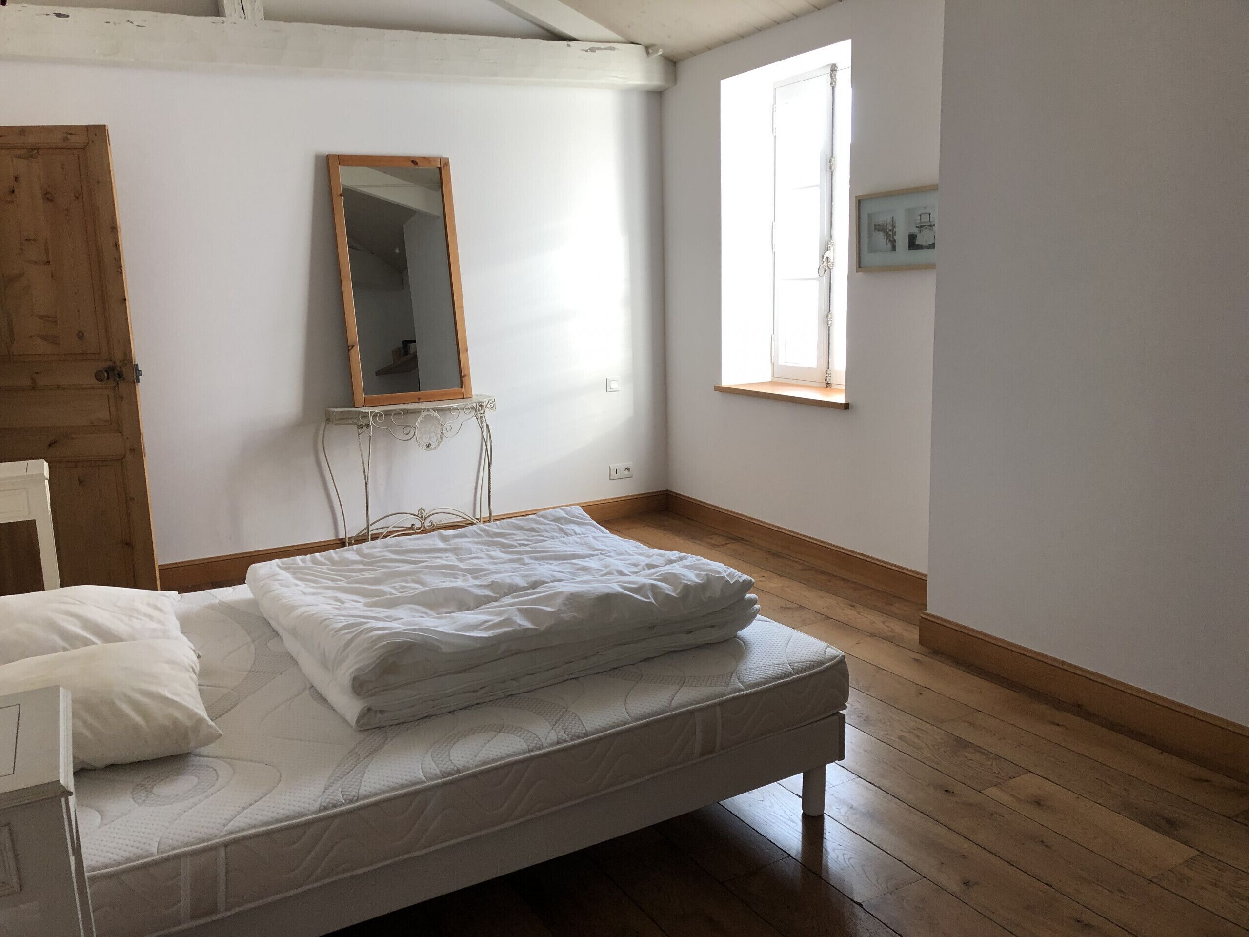 Een slaapkamer met een houten bed, een spiegel, een raam en een deur.