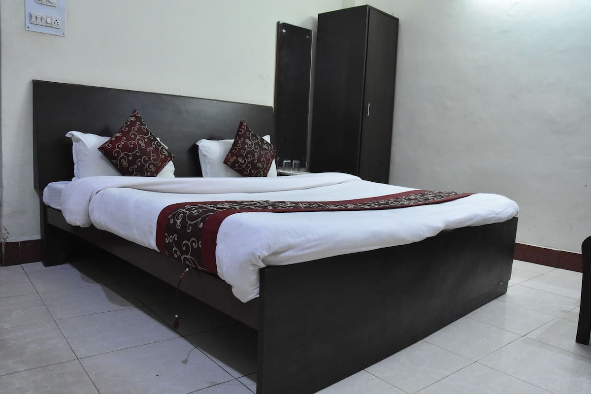 A double bed with white linens and two decorative pillows, a dark headboard, and a wardrobe in a hotel room.