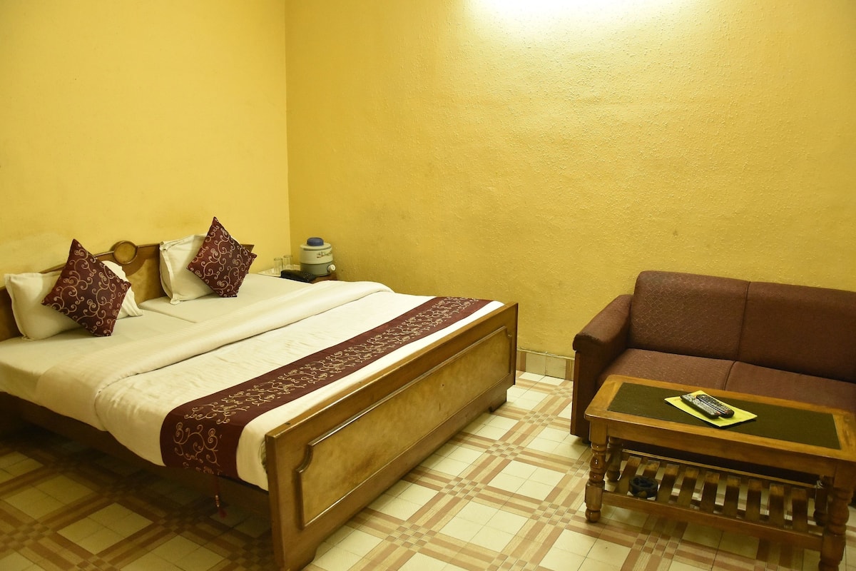 A bedroom with a bed, a sofa, a nightstand, and a water dispenser.