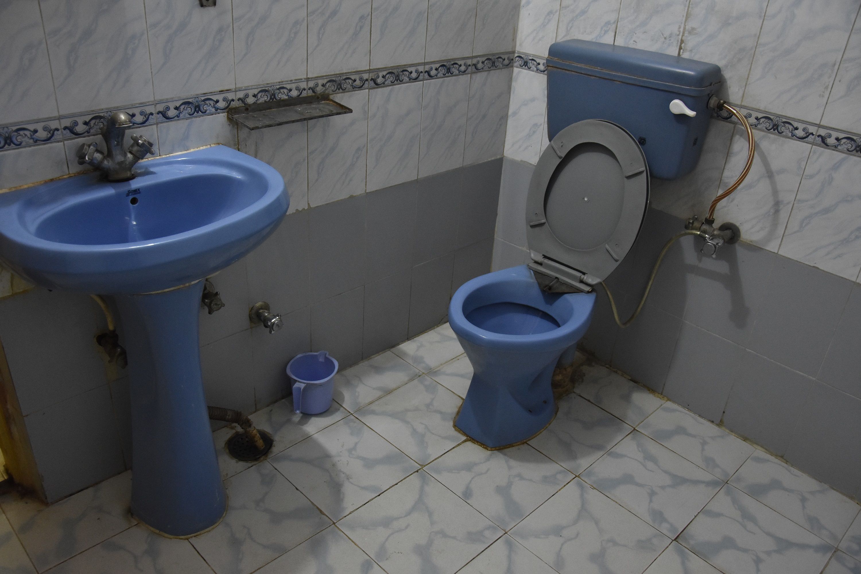 A bathroom with a blue sink, a toilet, and a small shelf.