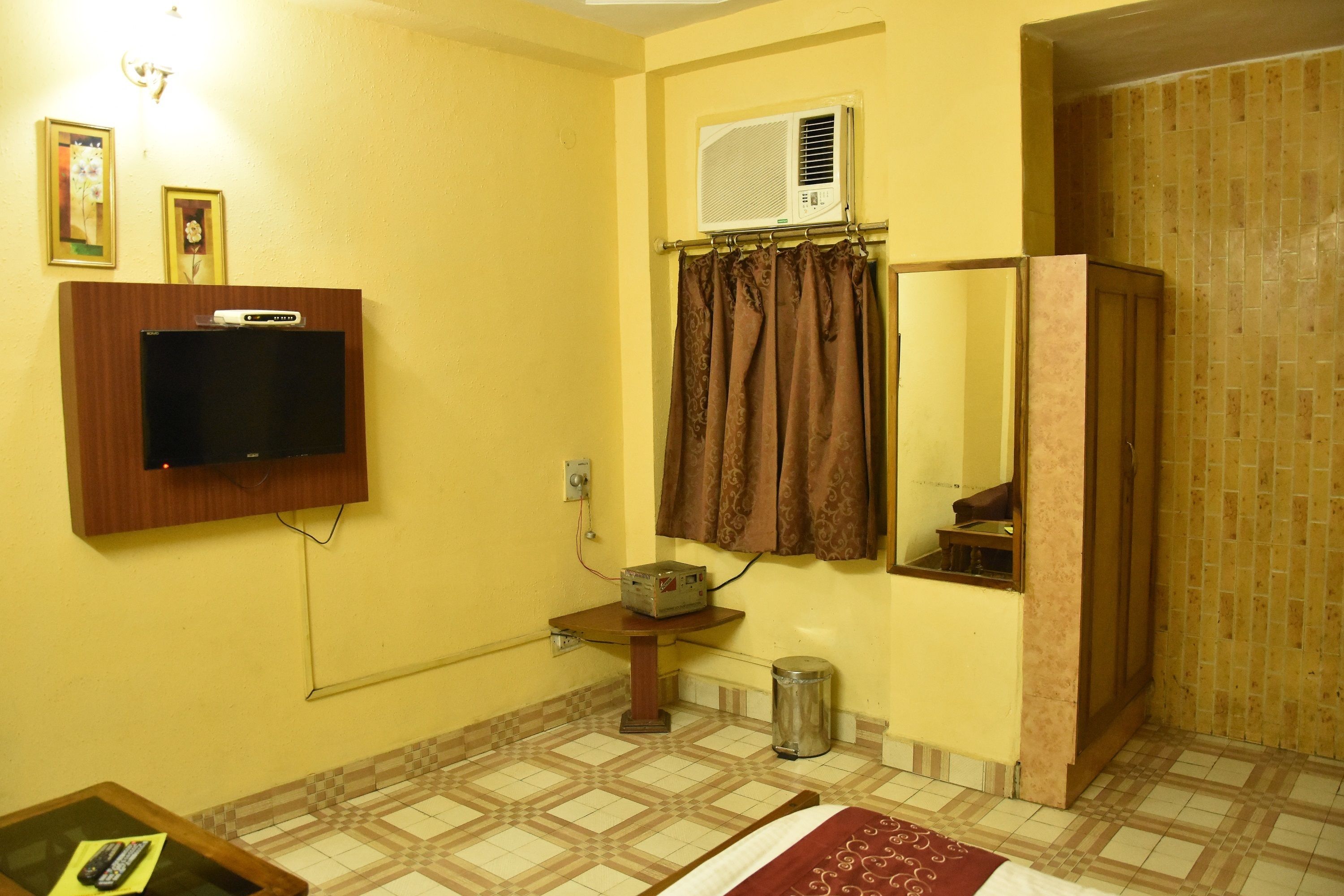A bathroom with a tiled floor, a shower area, a toilet, a sink, a mirror, and a television mounted on the wall.